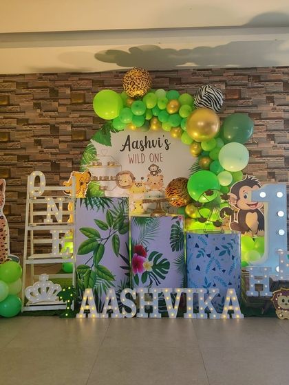 A 'Wild One' jungle safari theme with a leopard cutout, tropical print plinths, and a green and gold balloon garland.
