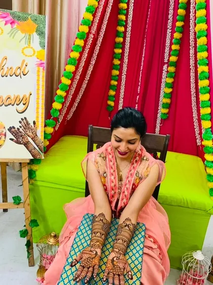 A happy bride at her mehndi ceremony, proudly displaying her full bridal henna on both hands.