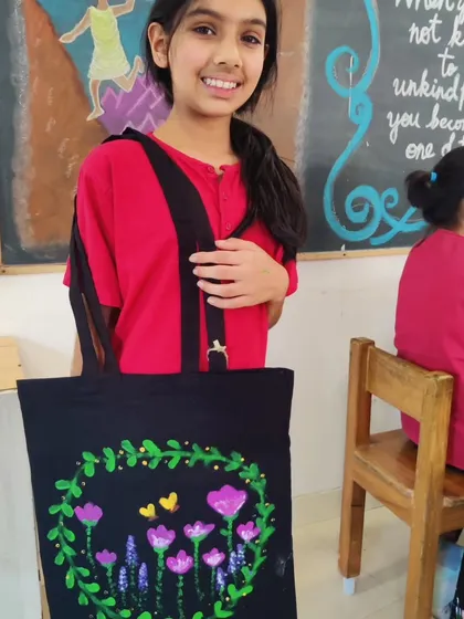 A girl shows off her tote bag, which she decorated with a beautiful wreath of purple flowers and yellow butterflies. This craft workshop encourages both artistic skill and personal expression.
