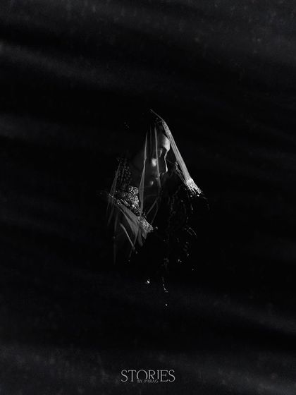 A fine art portrait in black and white, shrouded in shadow. The bride, with a veil over her head, is captured in a moment of quiet contemplation, creating a mysterious and timeless image.