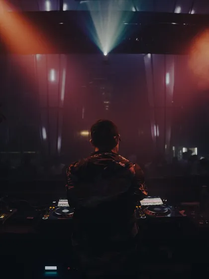 A powerful, atmospheric shot from behind, facing a massive light rig and a dark, expectant crowd. This captures the calm before the storm, the moment before I drop the next track.