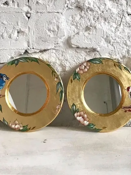 A pair of round mirrors framed with decoupage art. In our workshops, you'll learn how to smoothly apply designs to various objects, like these decorative wall hangings.