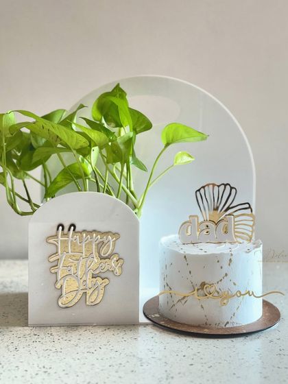 A beautiful shot of the white acrylic hamper for Father's Day. It comes with a hydroponic pothos plant and a matching white and gold cake, creating a coordinated and thoughtful gift set.