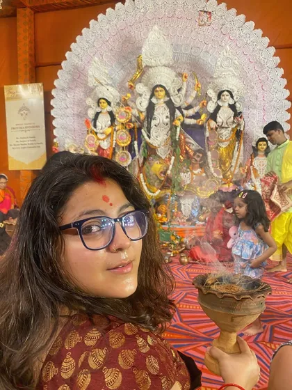 A moment of peace amidst the festivities. A woman holds the dhunuchi, looking towards the camera with a serene expression and a bindi on her forehead.