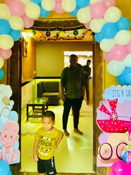 A gender reveal themed entrance inside a home, with 'It's a Boy' and 'It's a Girl' cutouts and a pastel balloon arch.