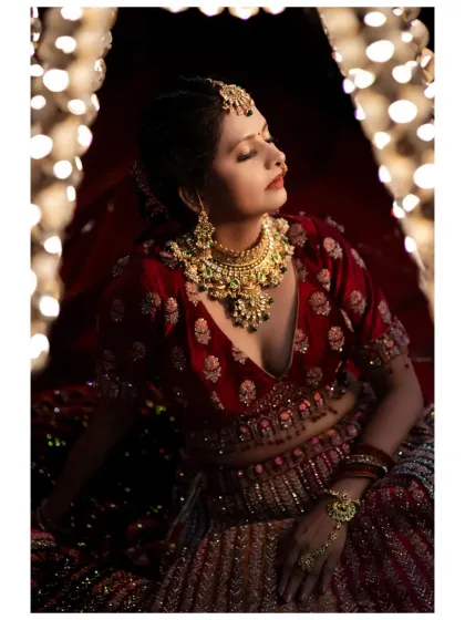A dramatic bridal portrait using warm, focused light. The bride, in a rich red lehenga, looks absolutely radiant and serene.