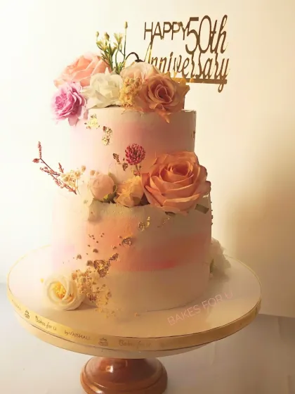 A stunning two-tier cake celebrating a 50th wedding anniversary. The soft watercolor finish, fresh flowers, and gold leaf accents create a beautiful and romantic centerpiece.