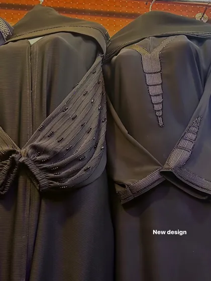 A close up of new abaya designs in a dark, charcoal grey. The details include intricate sleeve beading and textured fabric on the neckline and cuffs.