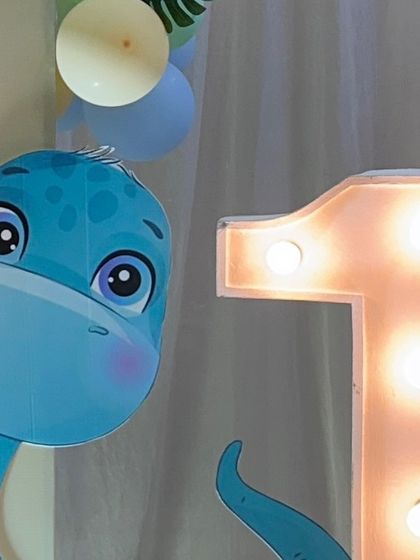 A close-up of a cute dinosaur cutout next to a light-up marquee number '1'. This is a perfect combination for a first birthday party with a dinosaur theme.