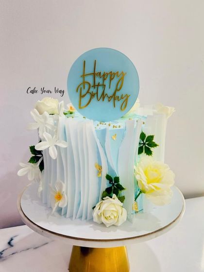 Celebrate in style with this beautiful blue and white cake, featuring wafer paper sails and fresh flowers.