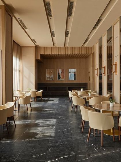 The banquet hall at Rustomjee Elements, showcasing the interplay of light and shadow from the large glass facade. The design embraces the trapezoidal floor plan, using the ceiling profile and furniture layout to create a dynamic space.