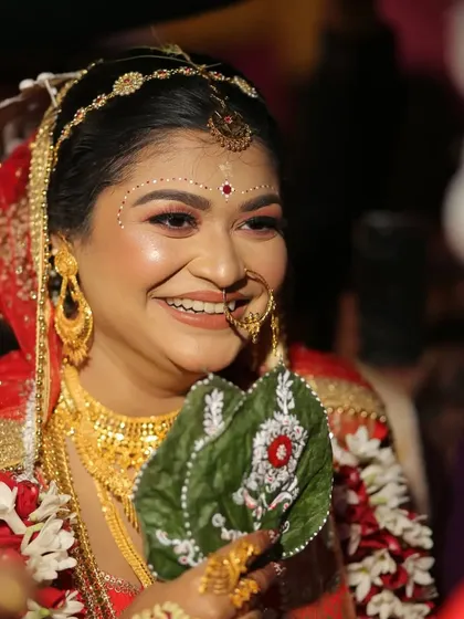 A beautiful Bengali bride holds a hand-painted paan leaf, her smile showing the joy of the moment. This small custom detail adds so much personality to the ceremony.