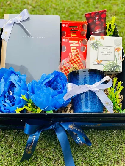 A custom Bhai Dooj curation for a brother, designed in a striking blue theme. This gift box includes a journal, chocolates, a face moisturizer, and a scented candle, adorned with deep blue flowers.