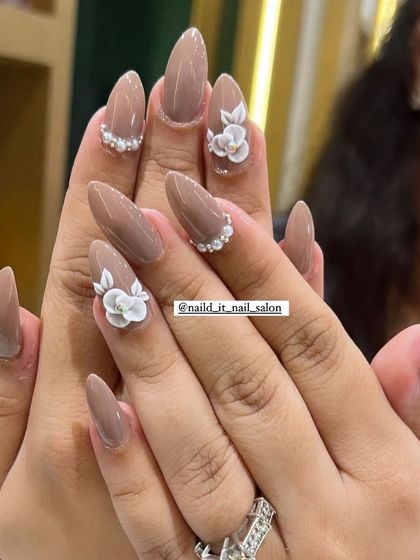 An elegant and understated bridal option. These almond-shaped nails are painted in a chic nude tone, with delicate 3D white flowers and pearl accents for a touch of sophistication.
