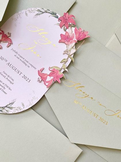 A stunning die-cut invitation for a wedding in Portugal. The card is shaped like an arch and features a cascade of 3D, hand-applied pink lilies, creating a truly unique and artistic piece.
