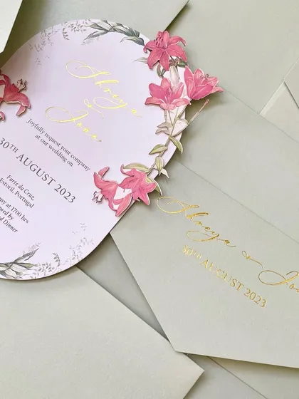 A stunning die-cut invitation for a wedding in Portugal. The card is shaped like an arch and features a cascade of 3D, hand-applied pink lilies, creating a truly unique and artistic piece.