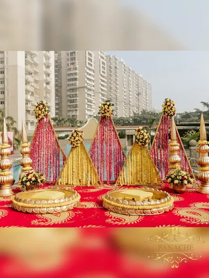 The main seating area for the Haldi ceremony, featuring traditional golden urlis and a backdrop of triangular panels adorned with marigold and rose petals.