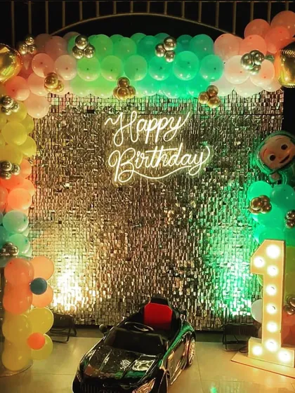 A Cocomelon themed first birthday with a silver shimmer wall. The setup also includes a toy car for the birthday boy, adding a fun element to the decor.