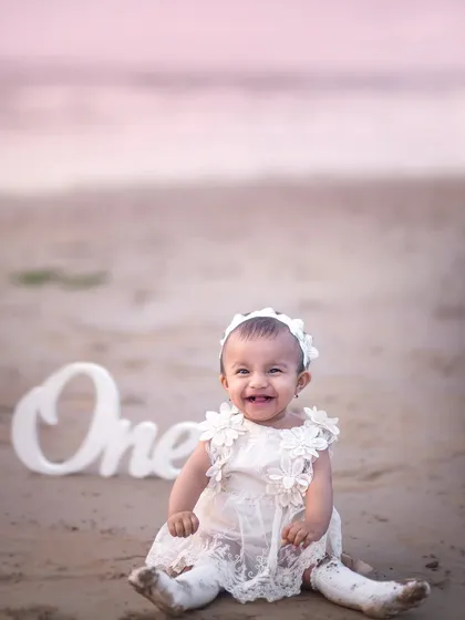 A first birthday celebration on the beach. The simple "One" prop and the baby's happy smile are all that's needed to mark this special milestone.