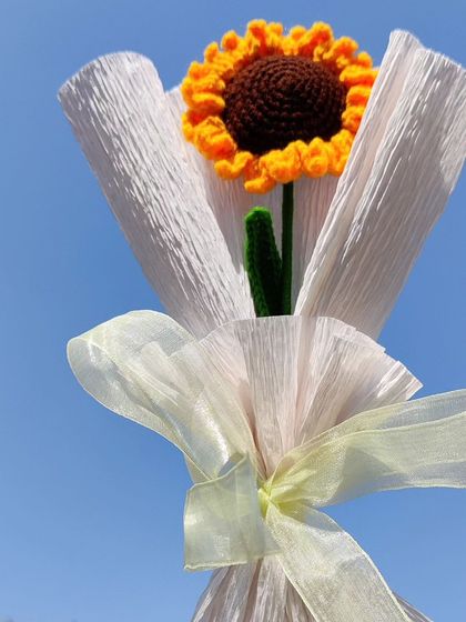 The single sunflower bouquet held against a blue sky.