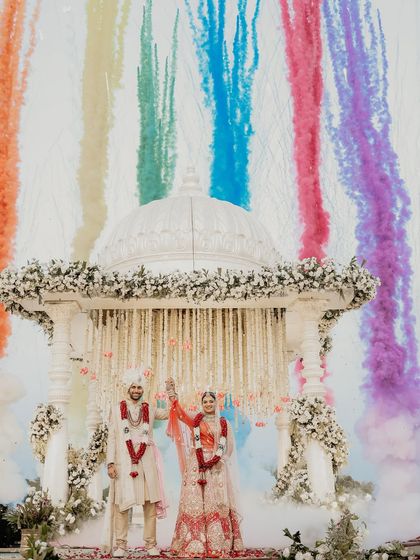 A spectacular celebration of union. As the couple stands united under the mandap, a rainbow of colored smoke erupts behind them, creating a truly unforgettable and vibrant wedding photograph.