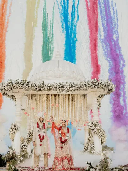 A spectacular celebration of union. As the couple stands united under the mandap, a rainbow of colored smoke erupts behind them, creating a truly unforgettable and vibrant wedding photograph.