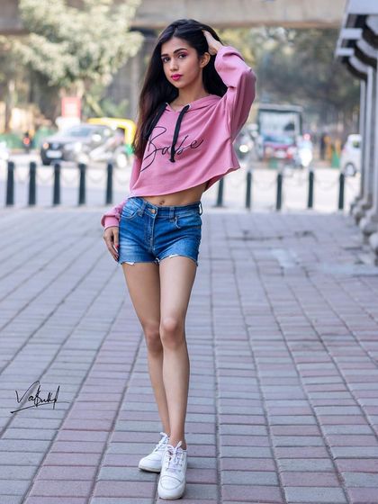 A full-length street style shot that captures the energy of the city. The model's pose is dynamic and confident, showcasing a trendy, casual outfit against a busy street backdrop.