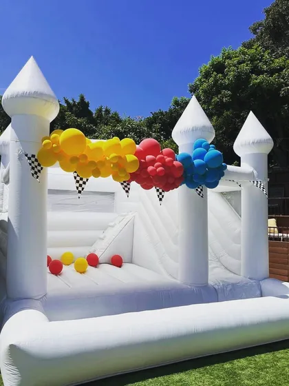 Our elegant white bouncy castle, shown here with a slide and ball pit, is a versatile choice for any event, from birthdays to more formal gatherings. It can be decorated with balloons to match your party's theme.