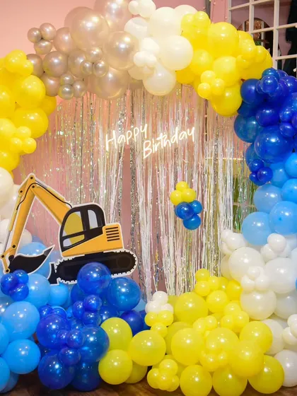 Another view of the impressive construction site decor, with a large excavator cutout and a full arch of yellow, blue, and white balloons.