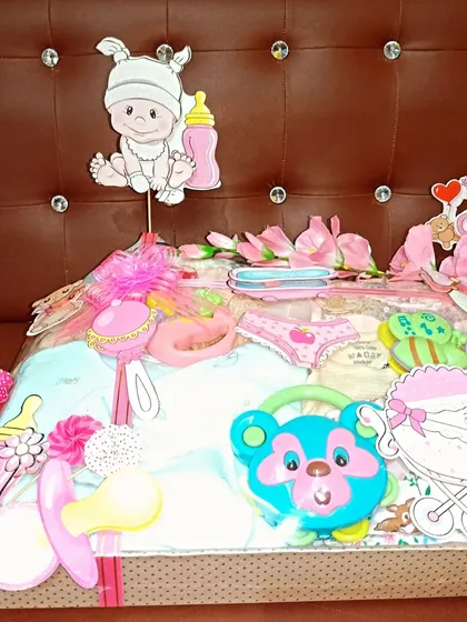 A beautifully decorated hamper for a baby girl, adorned with pink flowers and various baby-themed cutouts like pacifiers and strollers.