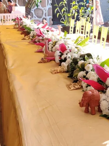 A close-up of the head table decor, showing a runner of white flowers and greenery, interspersed with small, decorative elephants and other traditional elements.