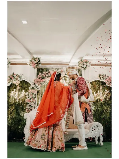 A wide shot of the wedding stage, capturing the grandeur of the ceremony. The couple stands before a beautifully decorated floral arch, ready to begin their new life together.