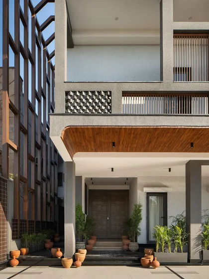 The entrance is framed by towering columns and a curved wooden canopy, softening the building's rugged exterior. Terracotta pots and lush greenery create a welcoming transition from the industrial cityscape.