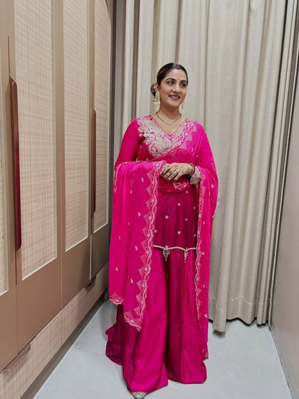 This pink sharara suit is perfect for a wedding guest. The dupatta is draped with a belt to create a modern, structured silhouette that is both stylish and easy to manage.