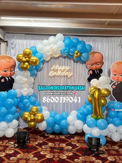 A Boss Baby theme for a first birthday celebration in a hall. This setup includes a ring of blue, white, and gold balloons with character cutouts.