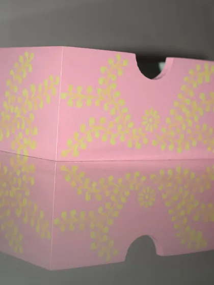 A side view of my hand-painted organizer, showing the delicate floral pattern against the pastel pink. The reflection highlights the smooth finish of this functional art piece.