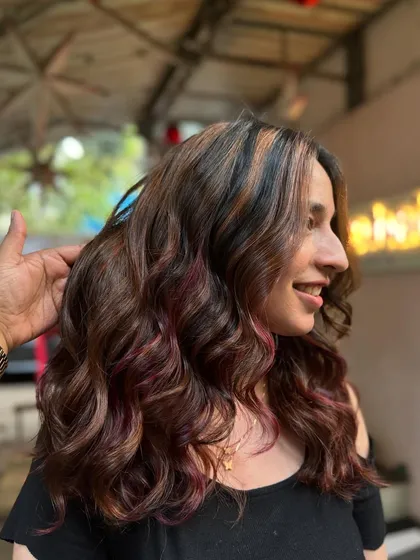 A happy client showing off her new hair. The subtle pops of color add a fun element to her beautiful brunette waves.