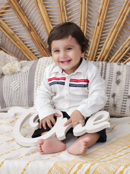 A happy one-year-old holding a wooden 'One' sign. This is a classic shot from my boho-themed first birthday sessions.
