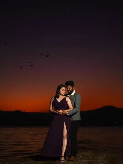 A wide shot capturing the couple against the vastness of the twilight sky. The deep orange and purple hues add a cinematic and epic feel to this romantic pre-wedding moment.