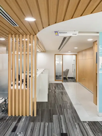 The reception area at Fortis Ludhiana combines a sleek Corian counter with a warm, wood-laminated ceiling. This blend of materials creates a modern yet inviting first impression for patients and visitors.