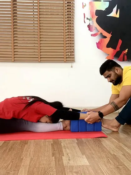 Using yoga blocks for an assisted forward fold (Paschimottanasana). This adjustment helps the student lengthen their spine and deepen the hamstring stretch without rounding the back.