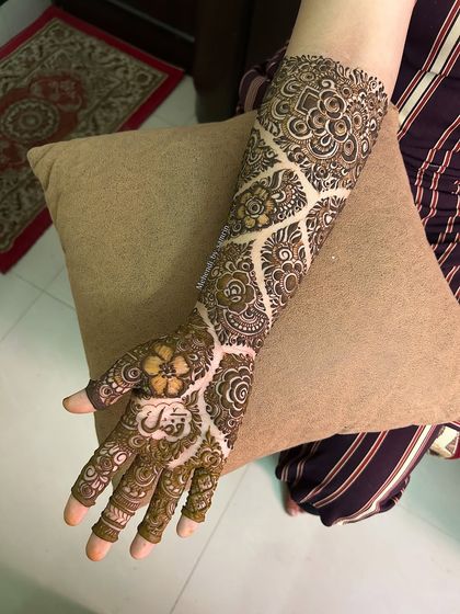A beautiful designer mehendi for an engagement bride. The pattern features a unique net or "jaal" design with floral motifs inside.