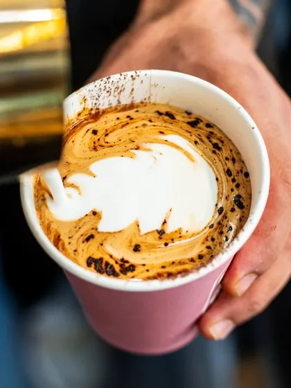 A barista pouring latte art into a takeaway cup. This action shot feels authentic and gives a glimpse into the daily craft at a coffee shop.