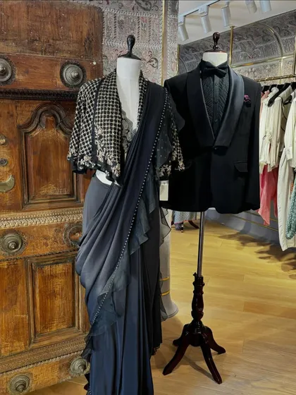A chic couple's look on display. The ruffled saree with a statement jacket for her and a classic black tuxedo for him is a perfect pairing for a modern reception.