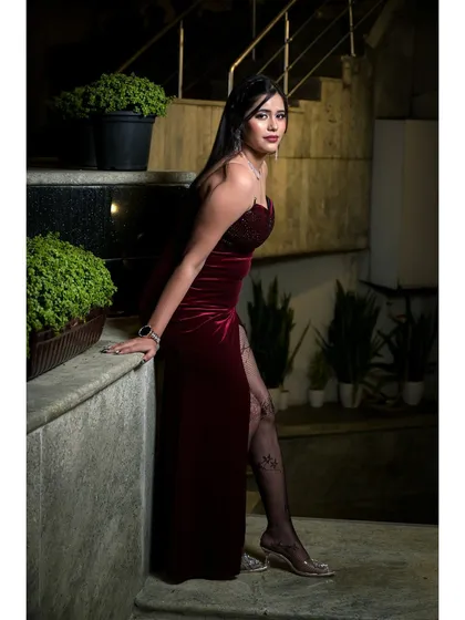 This portrait captures a glamorous and confident look. The pose, leaning against a stone ledge with soft lighting, highlights the elegance of the velvet dress and the model's poised expression.