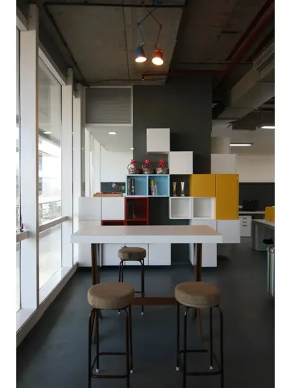 A high table by the window provides an alternative workspace. The design uses 'pixels' of storage in primary colors, a nod to the 8-bit gaming theme that runs through the entire office.