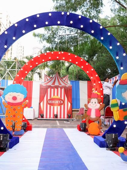 A wide shot of the carnival party entrance, showcasing the layered arches and playful character cutouts that create a sense of depth and excitement for arriving guests.