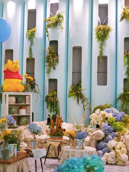 A comfortable seating area with a large Winnie the Pooh figure, floral-print sofas, and lush arrangements of hydrangeas and sunflowers.