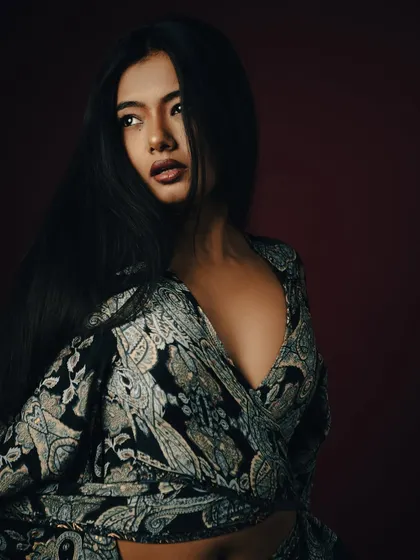 This shot captures the model in a classic pose, looking off-camera. The lighting highlights the texture of her hair and the pattern of the dress, creating a rich and sophisticated portrait with a touch of drama.