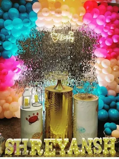 A colorful party with a silver sequin wall and a multi-colored balloon arch.